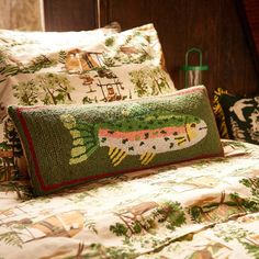 a bed topped with lots of pillows covered in green and pink designs next to a lamp