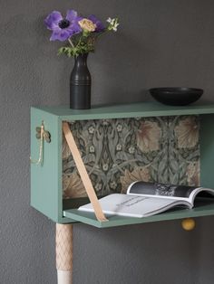 a vase with flowers and a book on a shelf next to a wall paper holder