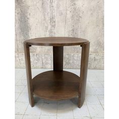 a round wooden table with one shelf on the top and two shelves below it, against a white tiled wall