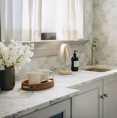 a kitchen counter with two coffee mugs on it and flowers in a vase next to the sink