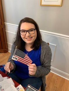 a woman sitting on the floor holding up an american flag and a book with other items around her