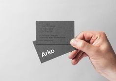 a person holding up two business cards with the word arko on them in white ink