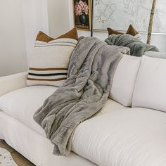 a white couch with two throw pillows on top of it and a blanket draped over the back