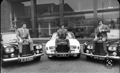 three men sitting on top of cars in front of a building