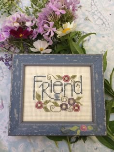 a cross - stitch picture frame with flowers and the word friend in it on a blue tablecloth