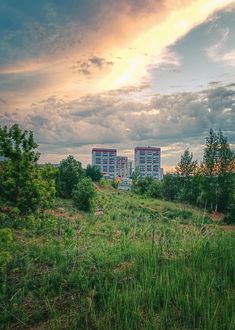 two tall buildings sitting on top of a lush green hillside under a cloudy blue sky