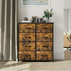 a wooden dresser with drawers in front of a painting on the wall next to a window