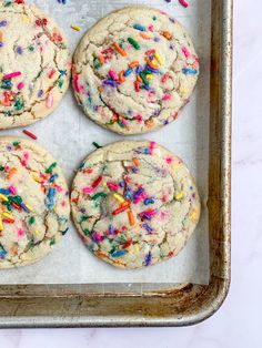 four cookies with sprinkles are on a baking sheet, ready to be baked