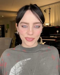 a woman with short black hair and blue eyes wearing a grey shirt in front of a piano