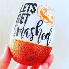 a hand holding an orange and white painted glass with the words let's get smashed on it