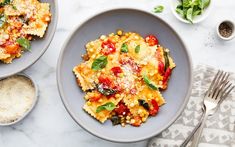 two bowls filled with pasta and vegetables on top of a white tablecloth next to silverware