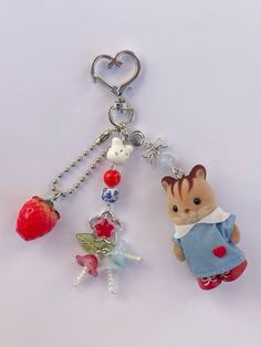 two keychains with charms attached to them on a white surface, one has a cat and the other is a strawberry