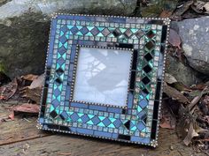 a blue and green mosaic photo frame sitting on top of a wooden table next to rocks