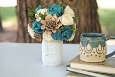 there is a vase with flowers in it next to a book and coffee mug on the table