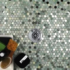 a bathroom with green and white mosaic tiles on the floor, including a shower faucet