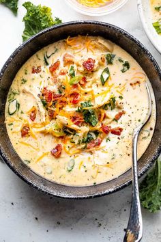 a bowl of soup with cheese, spinach and other ingredients on the table next to it