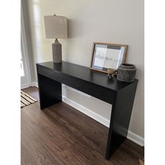 a black table with a lamp on it in front of a white wall and wooden floor