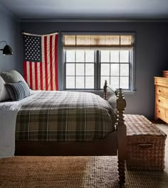 a bedroom with a bed, dresser and american flag hanging on the window sill