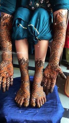 the legs and feet of a woman with henna tattoos on their hands, sitting on a blue cloth