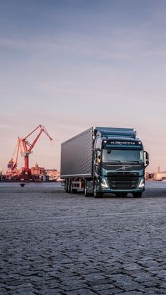 a semi truck is parked on the side of the road with cranes in the background