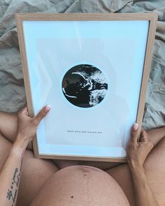 a pregnant woman is holding up a framed photo with her belly exposed and hands on the frame