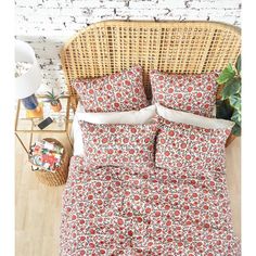 a bed with red and white flowers on it in front of a wicker chair