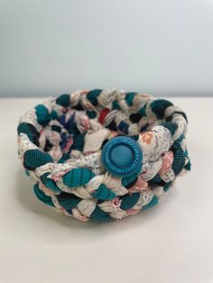 a close up of a bracelet on a white table with a blue button in the center