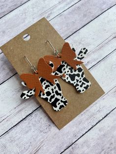 two pairs of cow print earrings on top of a piece of brown paper with black and white polka dots