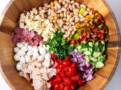 a wooden bowl filled with different types of vegetables and meat on top of each other