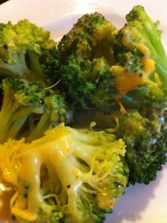 broccoli florets on a white plate with cheese drizzled over them