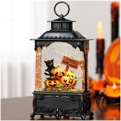 a lantern that has some pumpkins inside of it on top of a table next to candles