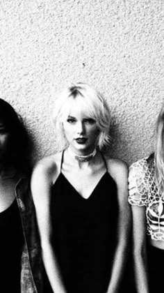 three women standing next to each other in front of a wall