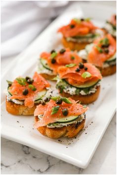 small appetizers with smoked salmon and cucumber on top are arranged on a white plate