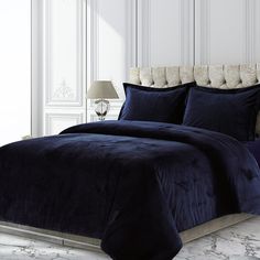 a bed with blue comforter and pillows in a white room next to a lamp