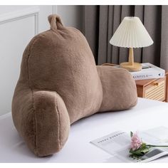 a brown pillow sitting on top of a white table next to a lamp and book