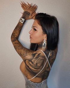 a woman with tattoos on her arms and shoulder is leaning against a wall wearing a silver dress