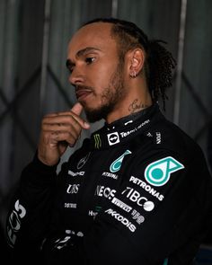 a man with dreadlocks standing in front of a wall wearing a racing uniform