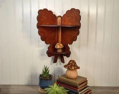 a wooden shelf with books, plants and an owl clock on it's side