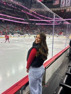 a woman standing in front of an ice rink with her arms around her back and smiling at the camera