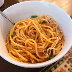 a white bowl filled with pasta and sauce on top of a table next to a cup