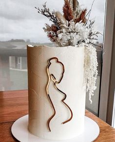 a white and gold wedding cake on a wooden table next to a window with flowers in it