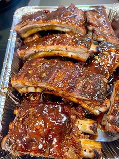 ribs covered in bbq sauce sitting on top of a pan filled with other meats