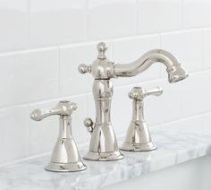 two chrome faucets sitting on top of a marble countertop next to a white tile backsplash