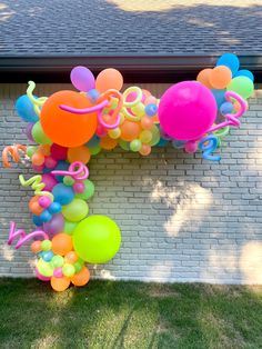 an arch made out of balloons and streamers in front of a brick wall,