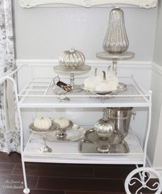 a white shelf filled with silver dishes and pumpkins