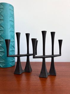 four black candlesticks sitting on top of a wooden table next to a blue vase