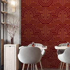 two white chairs sitting in front of a wall with red art deco design on it