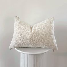 a white pillow sitting on top of a white table next to a white vase with flowers