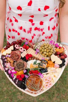 a woman holding a heart shaped platter filled with food