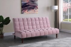 a pink futon sofa sitting in front of a window with a painting on the wall